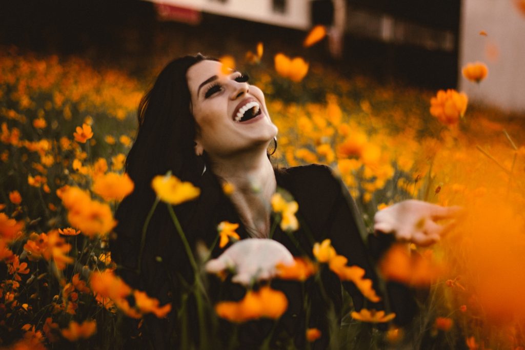 A woman laughing on flower field.Photo by Allef Vinicius